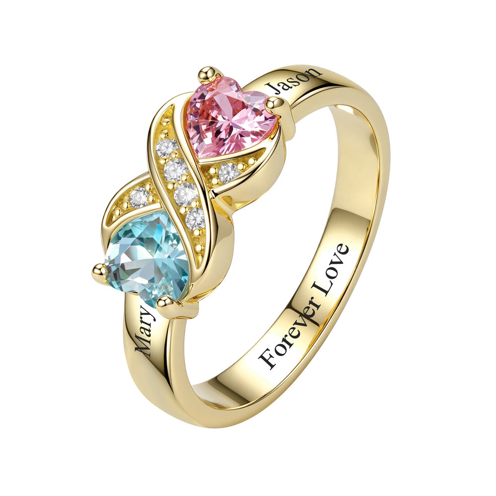 A gold custom birthstone infinity ring featuring a pink heart-shaped gemstone on one side and a light blue heart-shaped gemstone on the other, accented with small clear stones. The band is engraved with personalized names 'Mary' and 'Jason' and the phrase 'Forever Love'.