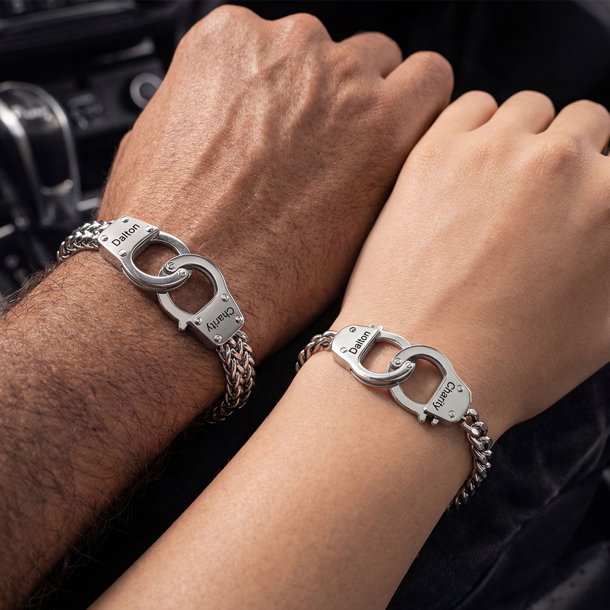 Two wrists wearing silver handcuff-style bracelets with visible branding.