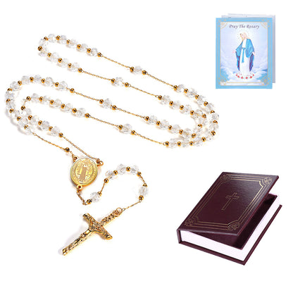 A Catholic rosary with clear crystal beads and a gold-tone crucifix and centerpiece, shown with a small prayer card and a dark brown leather-bound prayer book on a white background.