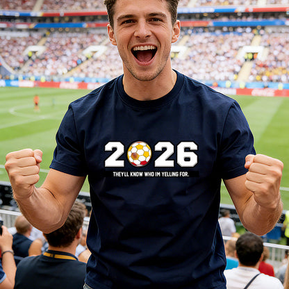 A Man wearing a navy blue t-shirt with '2026' wolrd cup text and soccer ball graphic, cheering in a stadium.