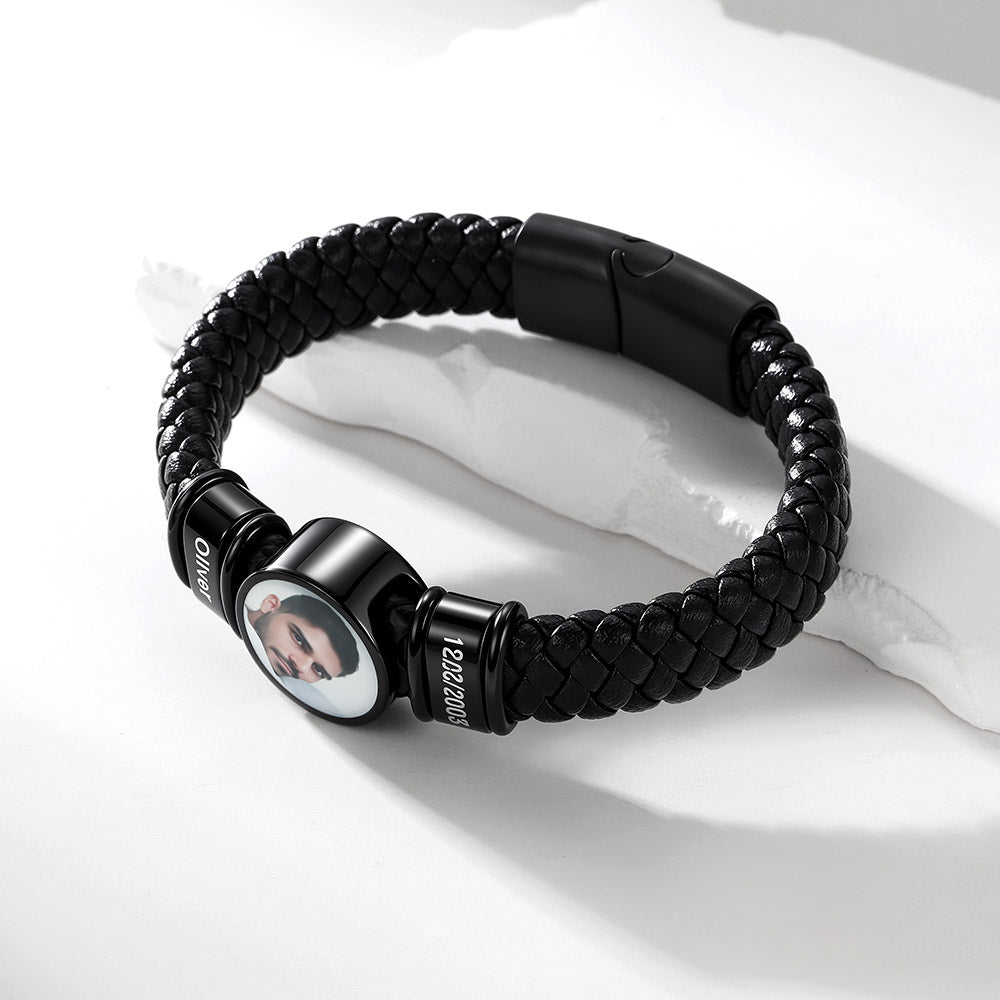 A black braided bracelet with a custom photo insert and black metal end caps, displayed on a white textured surface.