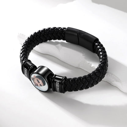 A black braided bracelet with a custom photo insert and black metal end caps, displayed on a white textured surface.
