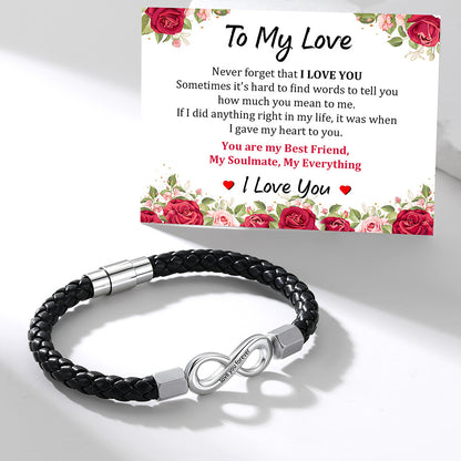 A black braided infinity bracelet with a silver infinity clasp is displayed in front of a matching floral 'To My Love' message card on a clean white background.