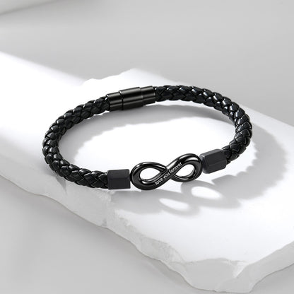 A black braided infinity leather bracelet with a matte black infinity symbol clasp engraved with 'I LOVE YOU', displayed on a white textured stone slab.