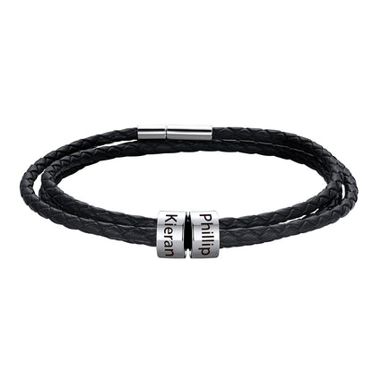 A black braided leather bracelet with two silver cylindrical nameplates engraved with the names 'Kieran' and 'Phillip', shown on a plain white background.