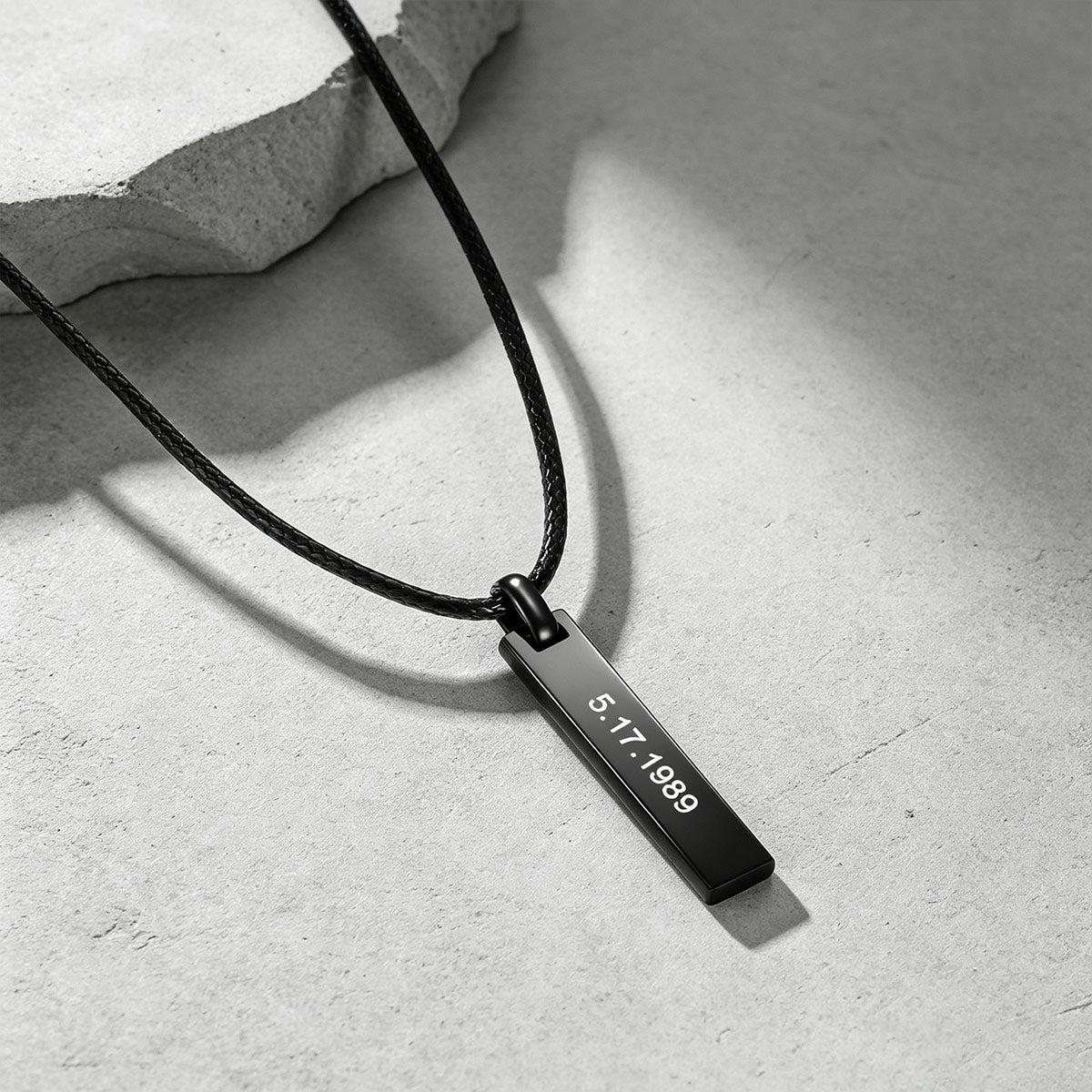 A black metal engraved bar necklace with a rectangular engraved tag reading '5.17.