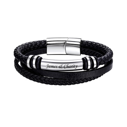 A black multi-layered leather bracelet featuring a braided wrap, a smooth leather band, and a polished silver-tone central cylinder engraved with 'James & Charity'. The bracelet is secured with a silver magnetic clasp and accented with black-and-silver spacer beads, shown on a plain white background.