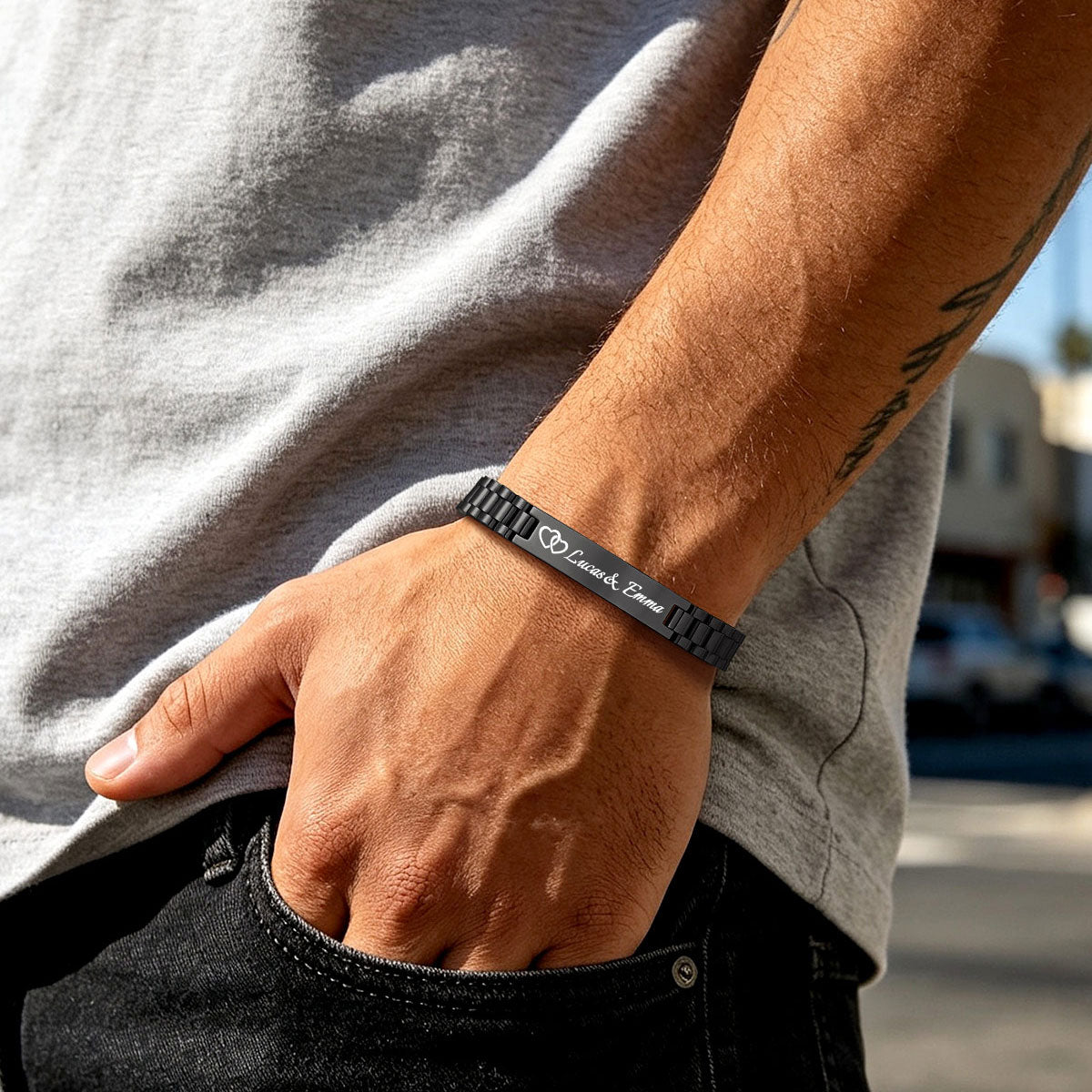 A close-up lifestyle shot of a man's wrist wearing a dark gray metal medical alert bracelet engraved with 'Drink Straight' and a cross symbol, paired with a gray t-shirt and black jeans.