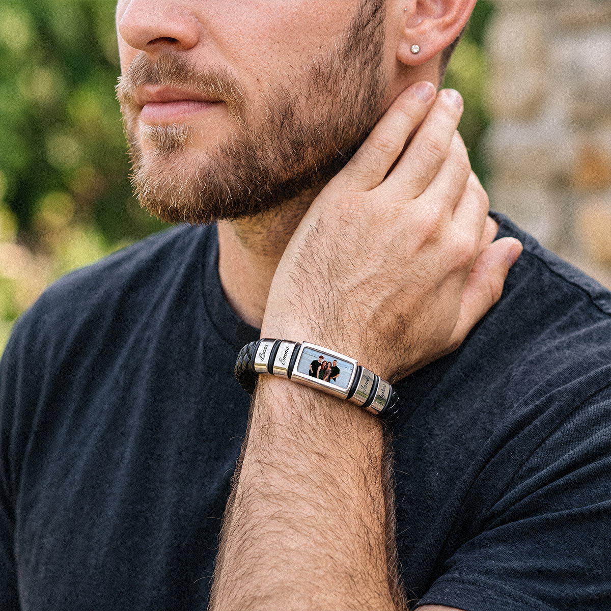 A close-up lifestyle shot of a man wearing a custom rectangularphoto leather bracelet on his wrist. The bracelet features a silver-toned metal frame with black and white striped silicone bands and a central custom photo insert.