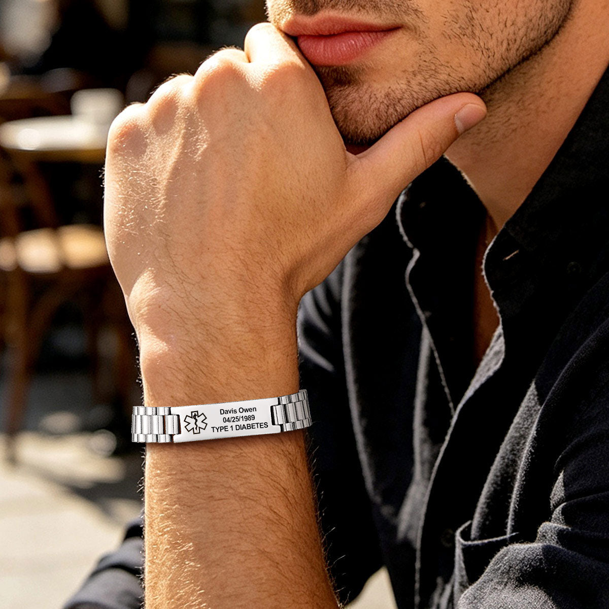 A close-up lifestyle shot of a man wearing a personalized silver medical alert bracelet on his wrist. The bracelet features a bicycle symbol and the engraved text 'David Owen 18.