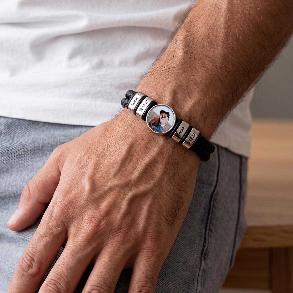 A close-up of a man's wrist wearing a personalized black photo leather bracelet with silver letter beads spelling 'LOVE' and a central oval photo charm.