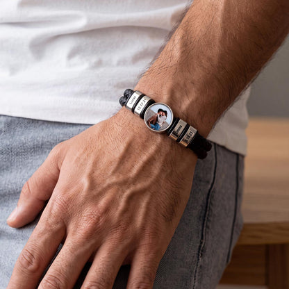 A close-up of a man's wrist wearing a personalized black photo leather bracelet with silver letter beads spelling 'LOVE' and a central oval photo charm.