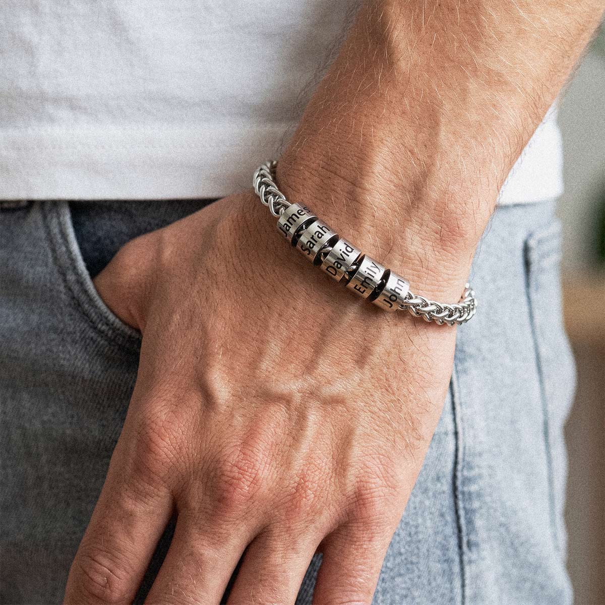 A close-up of a man's wrist wearing a silver-toned braided bracelet with three interlocking rotating numerals engraved with dates and names.
