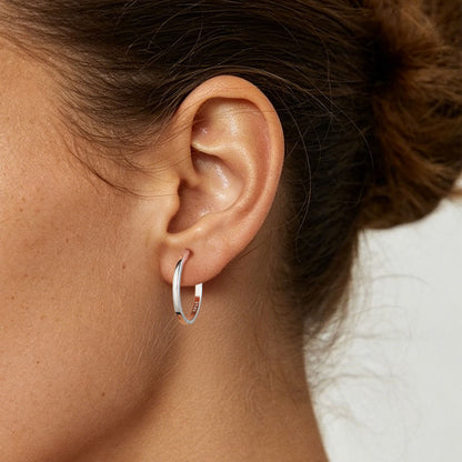 A close-up of a person's ear wearing a thin silver huggie earring.