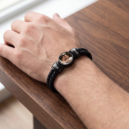 A close-up of a person's hand resting on a wooden table, wearing a black braided photo leather bracelet watch with a custom circular photo insert.