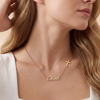 A close-up of a woman wearing a delicate gold chain name necklace with a small cross pendant and a personalized nameplate reading 'Clara'.