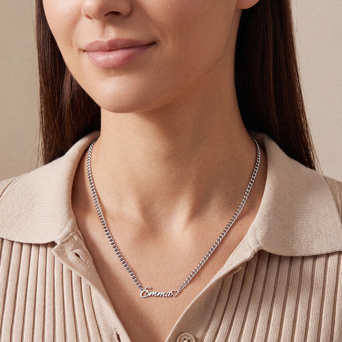 A close-up of a woman wearing a silver nameplate necklace that reads 'Emma' on a beige ribbed polo shirt.