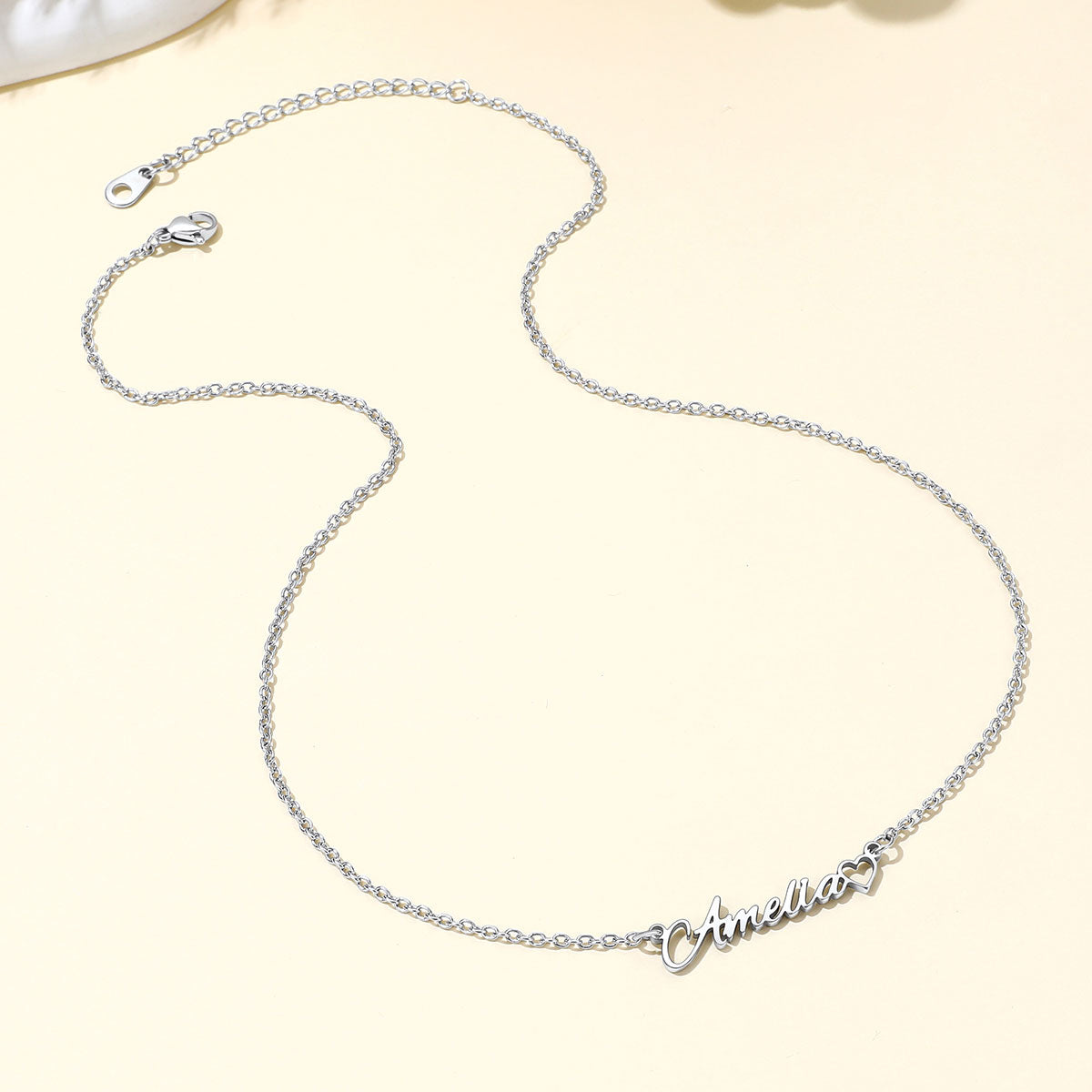 A delicate silver name necklace with a personalized script nameplate reading 'Annie' in a heart outline, displayed on a light cream background.
