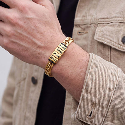 A gold-plated chain bracelet with three vertical nameplates engraved with 'Daniel', 'Mary', and 'James' in black text, worn on a man's wrist.