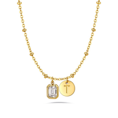 A gold chain birthstone necklace featuring a rectangular baguette-cut clear gemstone pendant and a round gold initial pendant engraved with the letter 'T', displayed on a clean white background.