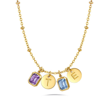 A gold chain birthstone necklace featuring four charms: two round gold discs engraved with letters 'T' and 'E', and two bezel-set rectangular gemstones in purple and light blue, each engraved with a letter.