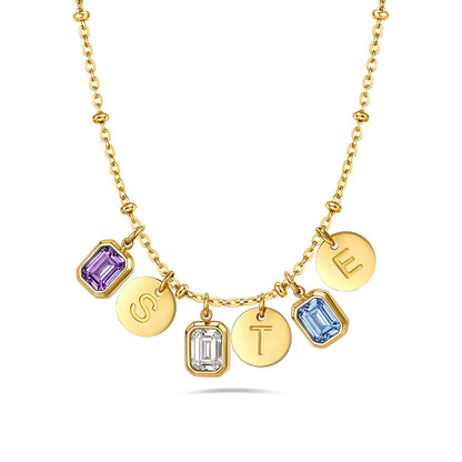 A gold initial birthstone necklace featuring five dangling charms spelling out 'STEL'. The charms include two round gold discs with engraved letters 'S' and 'T', one round gold disc with the letter 'E', one square bezel-set purple amethyst, and one square bezel-set light blue topaz, with one clear gemstone charm.