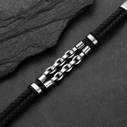 A men's bracelet featuring a black braided leather strap and a central silver-toned chain link design, displayed diagonally on a dark textured slate background.