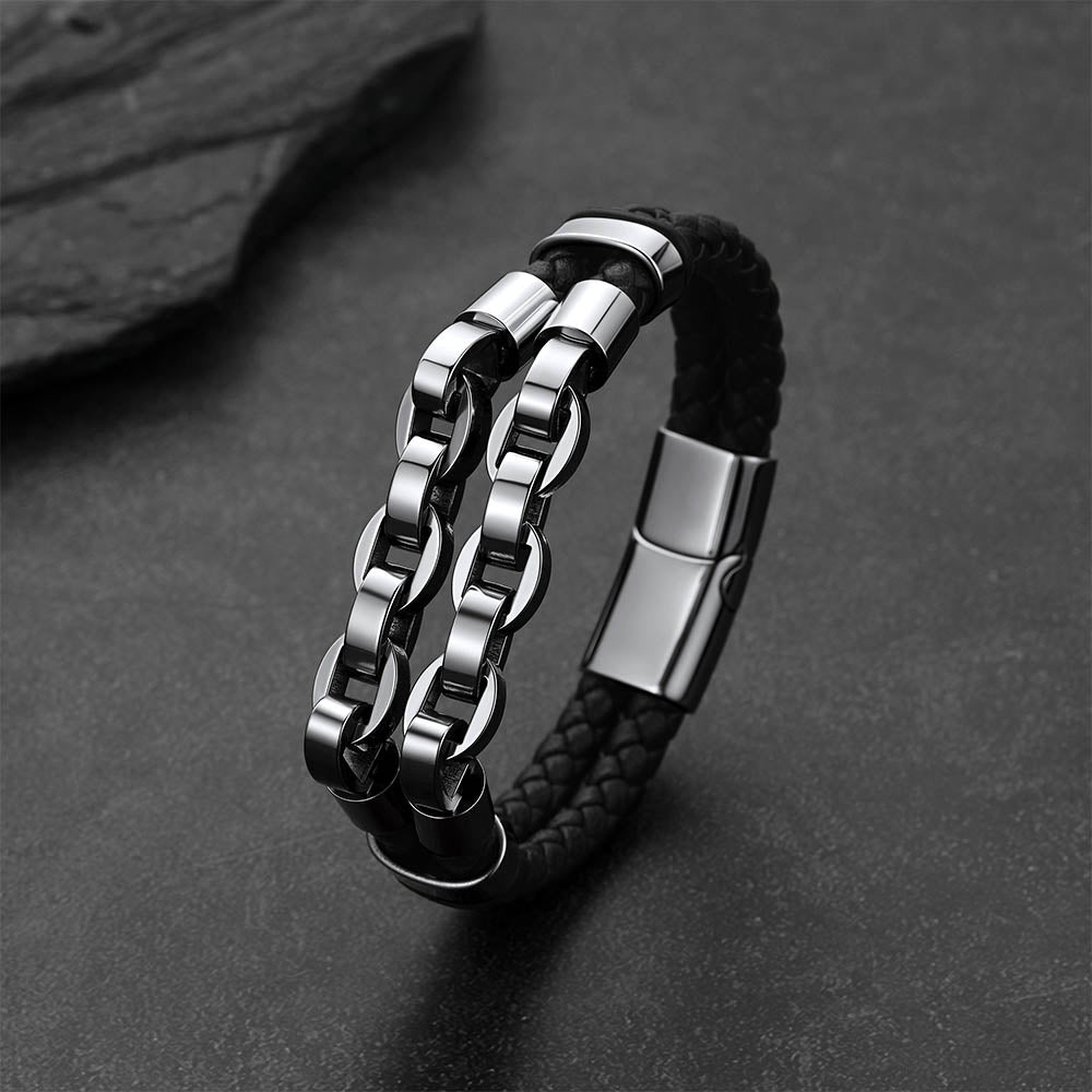 A men's double-strand bracelet featuring a black braided leather strap and a polished silver-tone stainless steel chain link design, displayed on a dark textured surface.