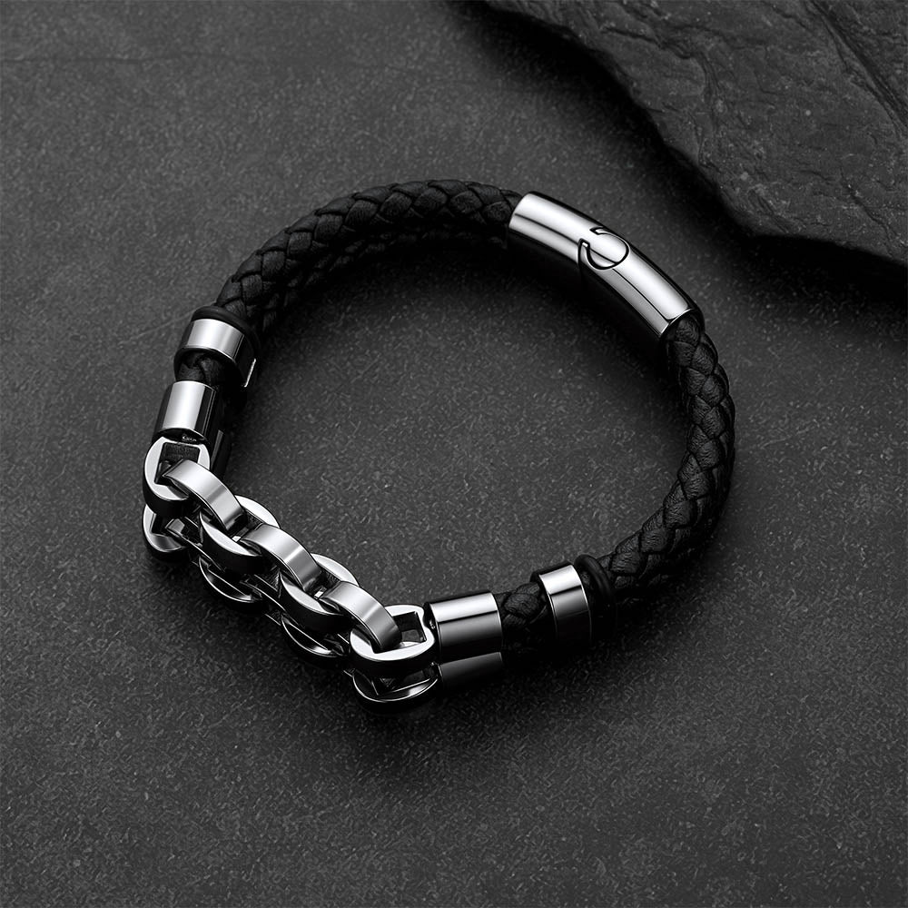 A men's link chain bracelet with a black braided leather wrap, featuring polished silver-tone metal accents and a sliding clasp, displayed on a dark textured slate background.