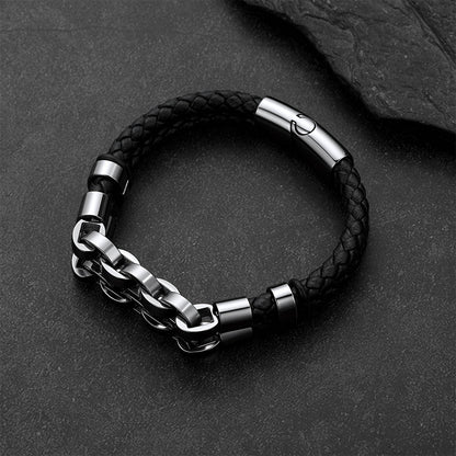 A men's link chain bracelet with a black braided leather wrap, featuring polished silver-tone metal accents and a sliding clasp, displayed on a dark textured slate background.