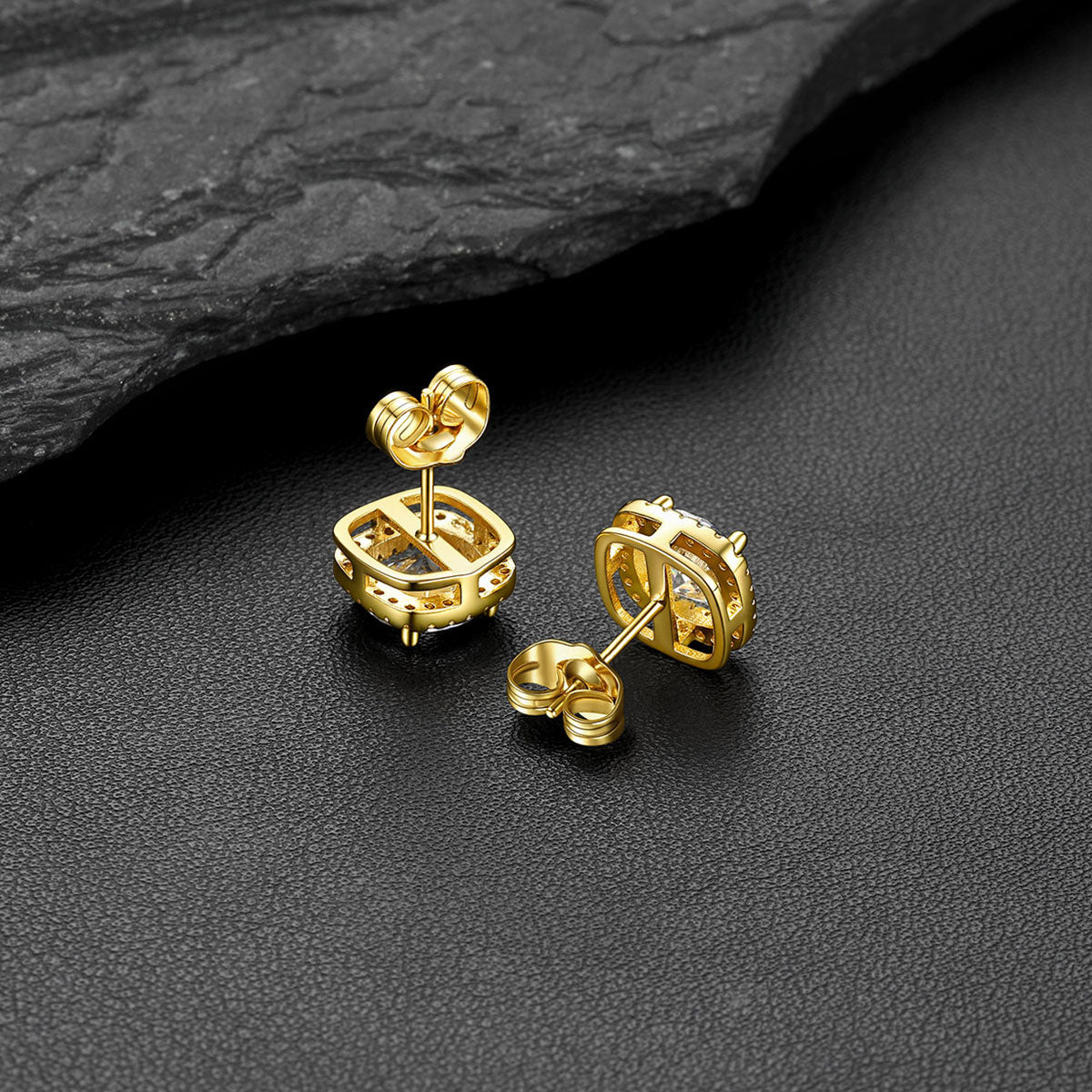 A pair of gold-toned cubic zirconia stud earrings with a cage-like openwork design, displayed on a textured black surface with a dark slate prop.