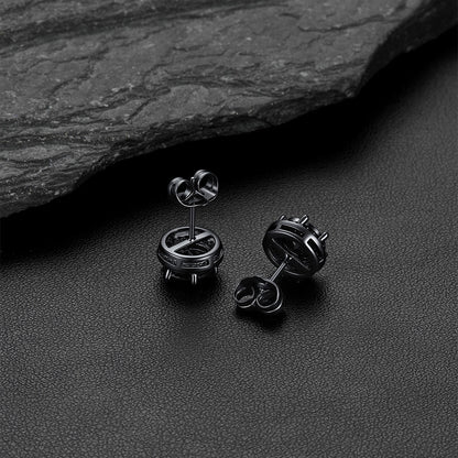 A pair of matte black CZ stud earrings, displayed on a dark textured surface with a slate stone in the background.