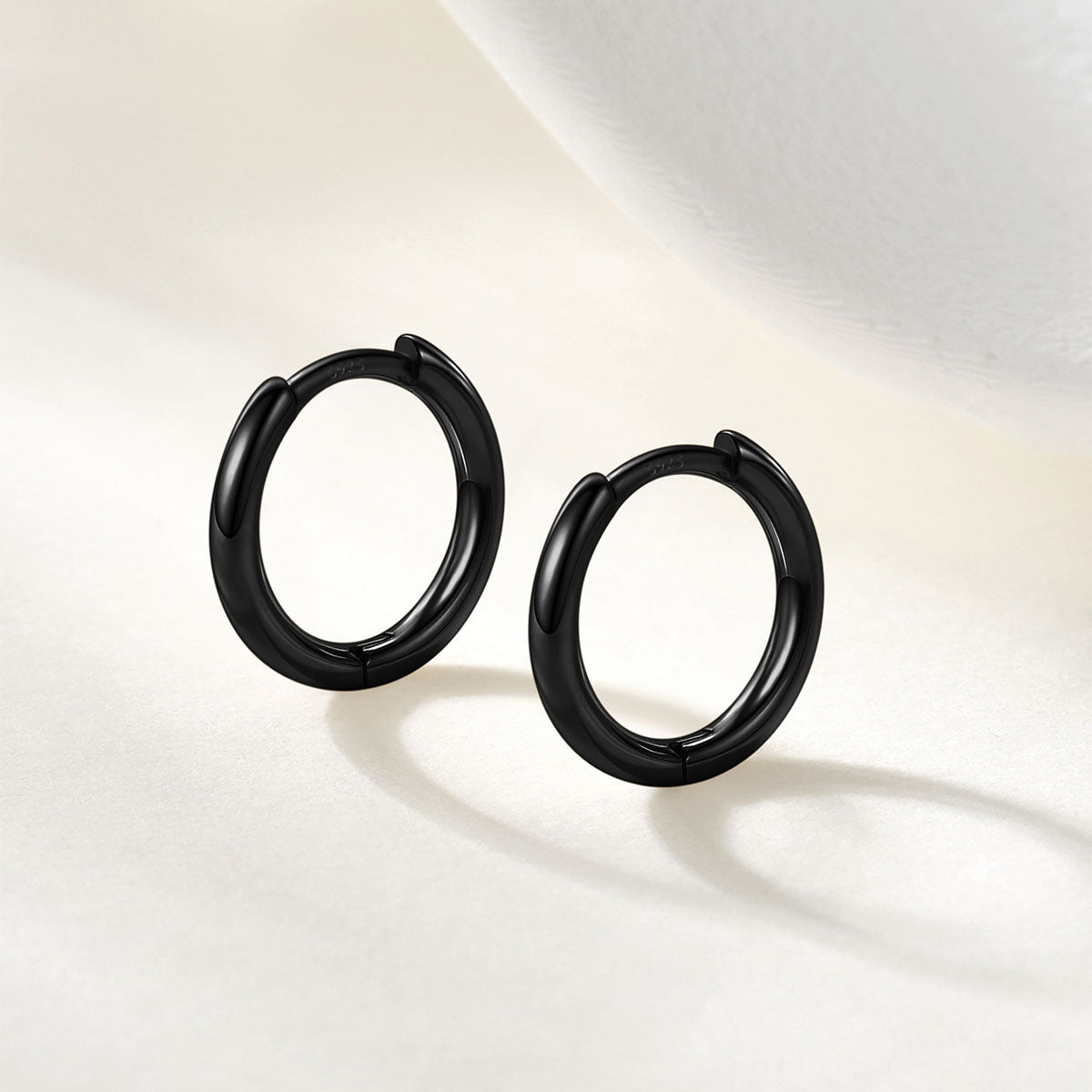 A pair of matte black hoop earrings displayed on a clean, light beige surface with soft shadows.