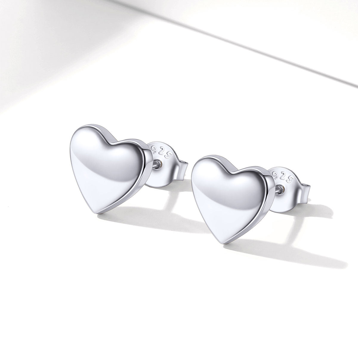 A pair of polished silver heart-shaped stud earrings with a reflective finish, displayed on a clean white surface with soft shadows.