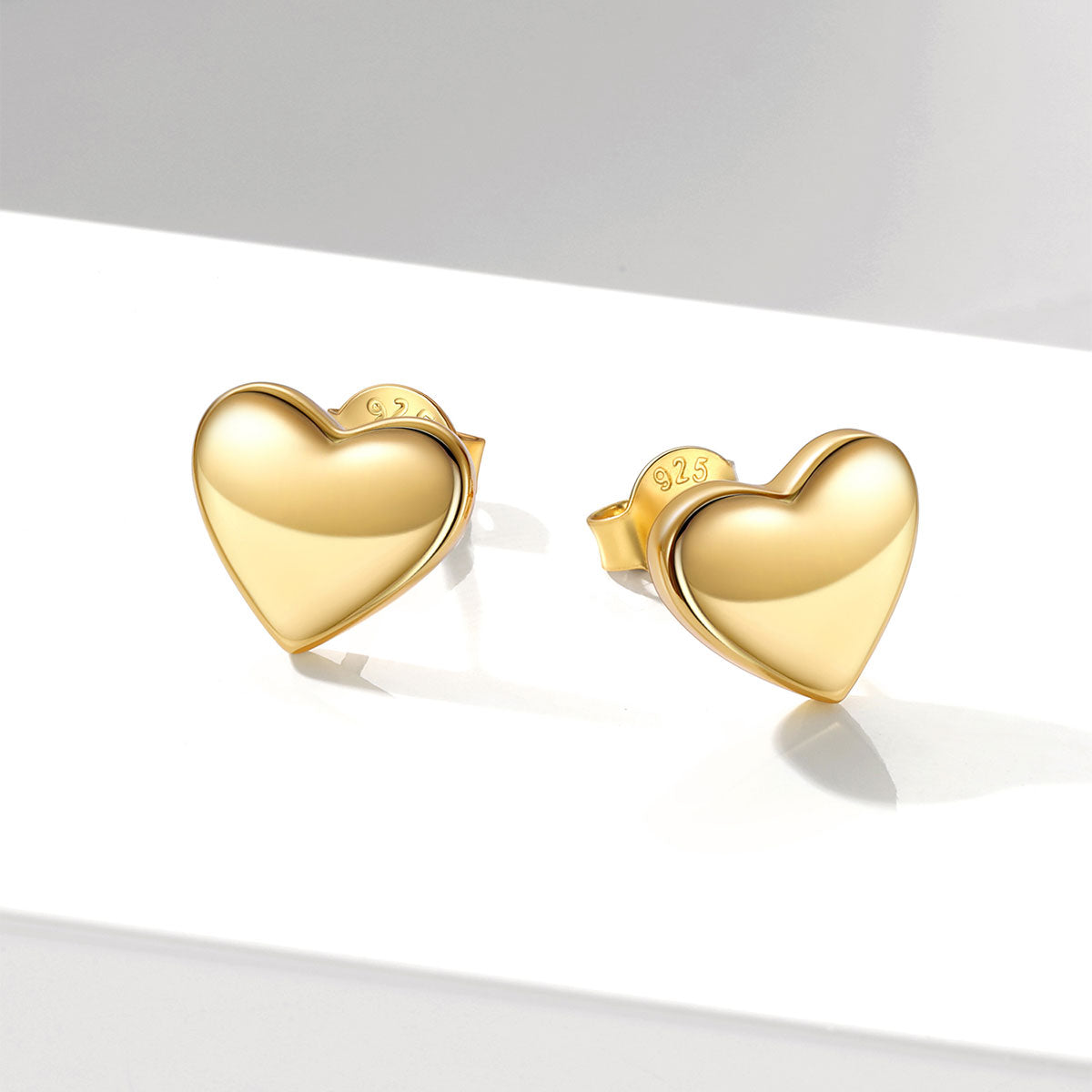 A pair of polished yellow gold heart-shaped stud earrings on a clean white surface with soft shadows.