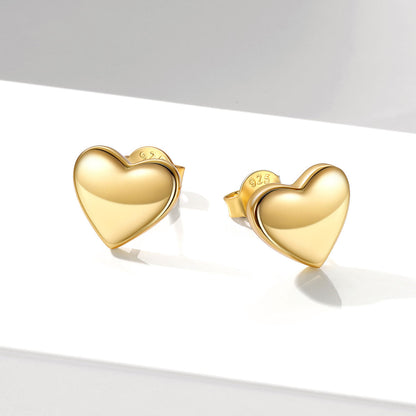 A pair of polished yellow gold heart-shaped stud earrings on a clean white surface with soft shadows.