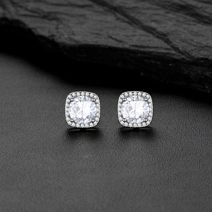 A pair of square cushion-cut CZ stud earrings with clear gemstones in a silver-toned setting, displayed on a dark textured surface with a black slate background.