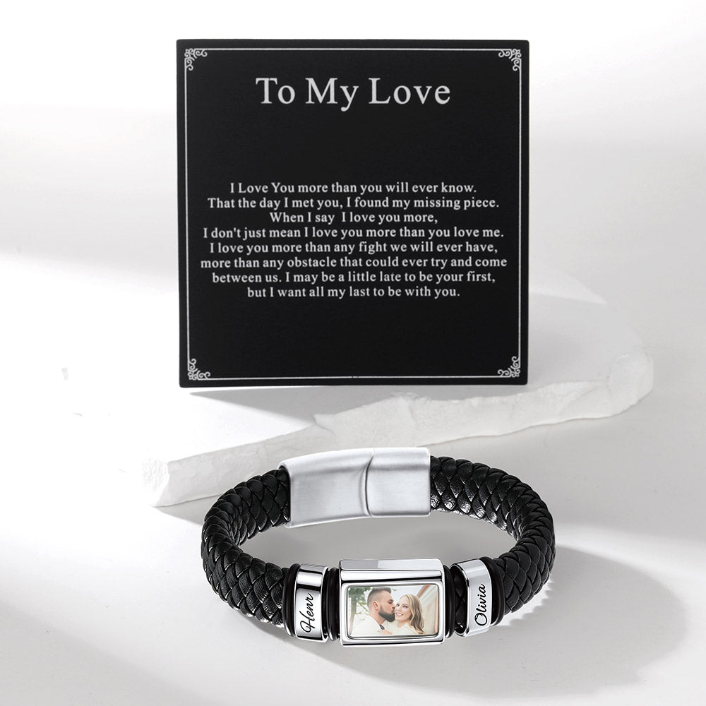 A personalized black braided bracelet with silver-toned metal accents, a photo frame in the center, and engraved nameplates, displayed in front of a black card that reads 'To My Love' with a sentimental message.