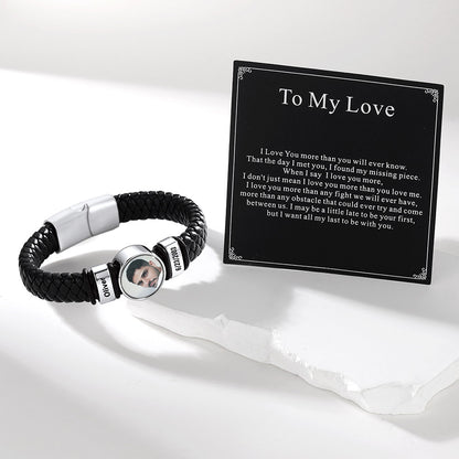 A personalized black braided cord photo bracelet with silver-toned metal accents and a circular photo charm, displayed next to a black printed card that reads 'To My Love' with a poem. The photo charm shows a man's face with the name 'James' on the side.