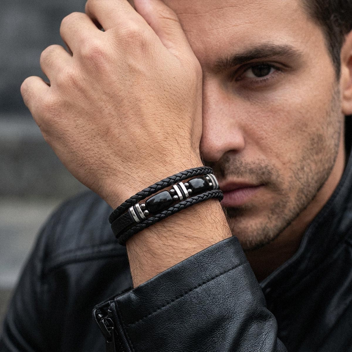 A close-up lifestyle shot of a man wearing a black braided leather bracelet with polished black and silver beads on his wrist, set against a dark gray background.
