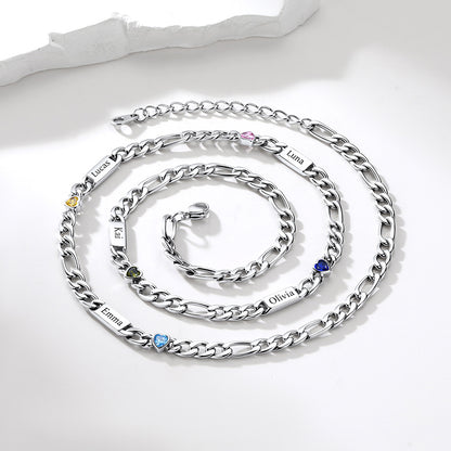 A silver-tone personalized chain necklace arranged in a spiral on a white surface. The necklace features multiple engraved name plates, including Emma, Olivia, Alex, Laura, and Noah, each accented with a small round gemstone in yellow, green, blue, pink, and purple.