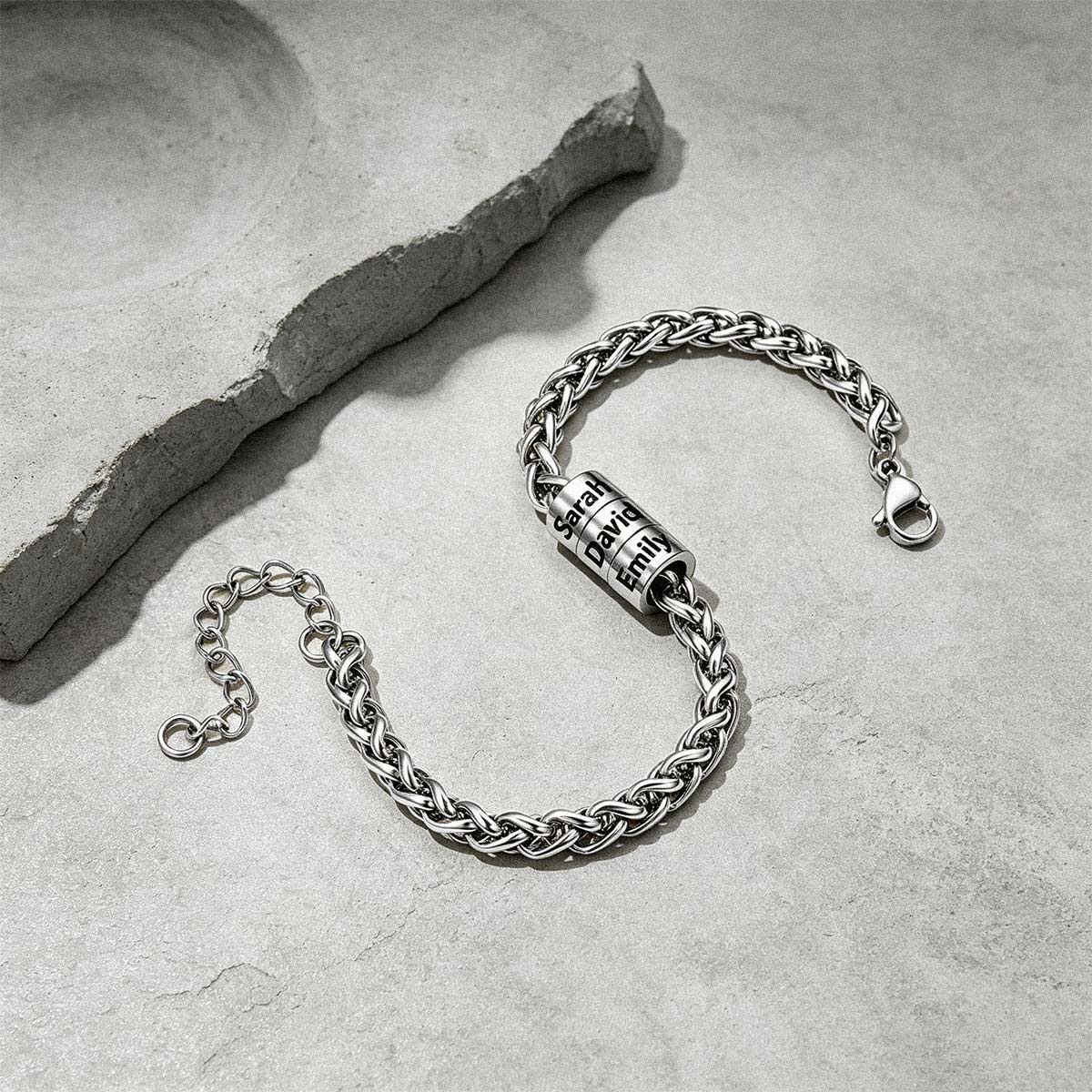 A silver-toned chain bracelet with a cylindrical lock charm engraved with the word 'FREEDOM', displayed on a textured gray stone surface next to a decorative slate piece.