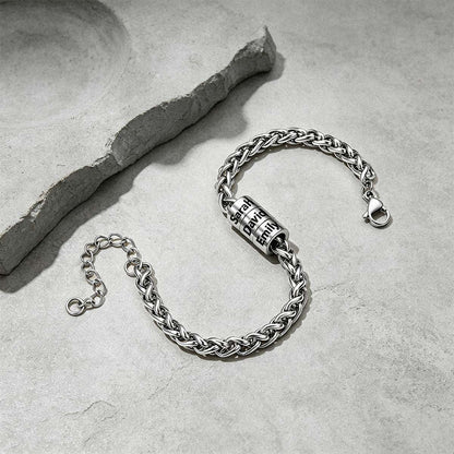A silver-toned chain bracelet with a cylindrical lock charm engraved with the word 'FREEDOM', displayed on a textured gray stone surface next to a decorative slate piece.