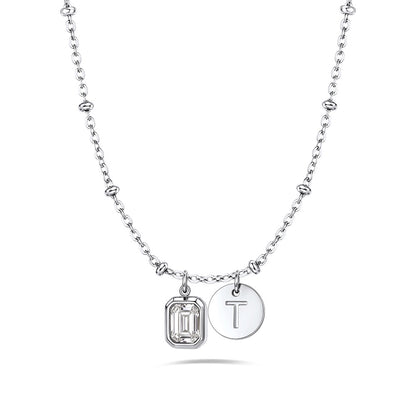 A silver birthstone initial necklace featuring a beaded chain, a rectangular bezel-set clear gemstone charm, and a round engraved silver disc charm with the letter 'T', shown on a clean white background.