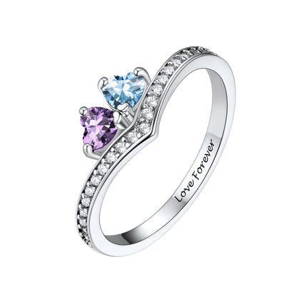 A silver birthstone ring featuring two heart-shaped gemstones, one light blue and one purple, accented by small clear stones along the band. The inside of the band is engraved with the words 'Love Forever'.