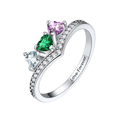 A silver heart-shaped birthstone  ring featuring three heart-shaped gemstones in green, purple, and clear, with small clear stones along the band and 'Love Forever' engraved inside. The ring is shown on a plain white background.