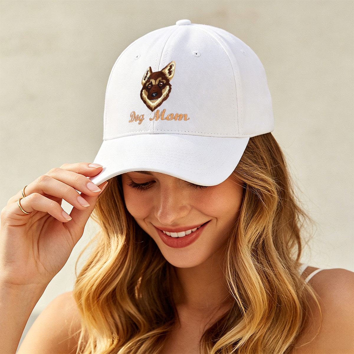 A woman wearing a white baseball cap with an embroidered German Shepherd dog face and the words 'Dog Moon' in tan script on the front. She is smiling and holding the brim of the cap against a soft beige background.