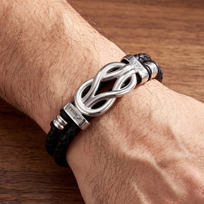 Black braided multi name leather bracelet with silver knot design on a wrist against a wooden background