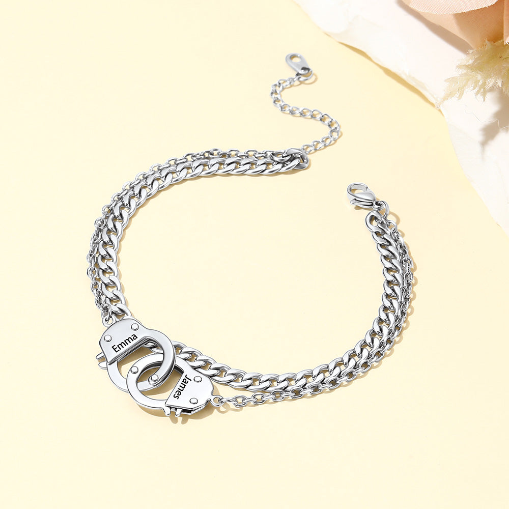 A silver-toned chain engraved handcuff ankle bracelet with a distinctive padlock clasp engraved with the name 'Emma', displayed on a pale yellow background.