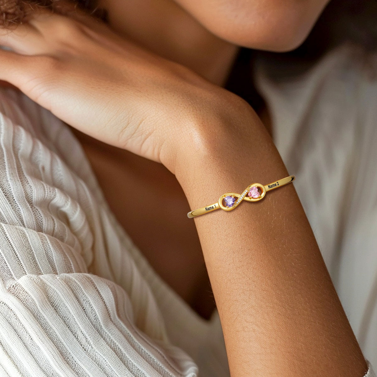 Gold infinity birthstone bracelet with colorful stones on a person's wrist against a neutral background